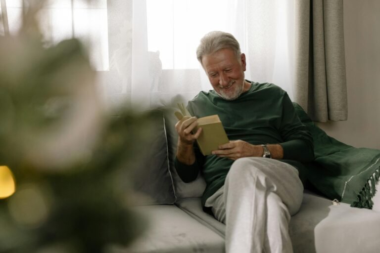 Senior man relaxing and reading a book on a sofa, enjoying the cozy holiday atmosphere indoors.